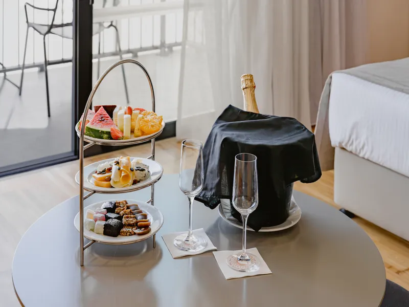 Three-tier stand of fruit, cheese and desserts beside a sparkling wine bucket in the room