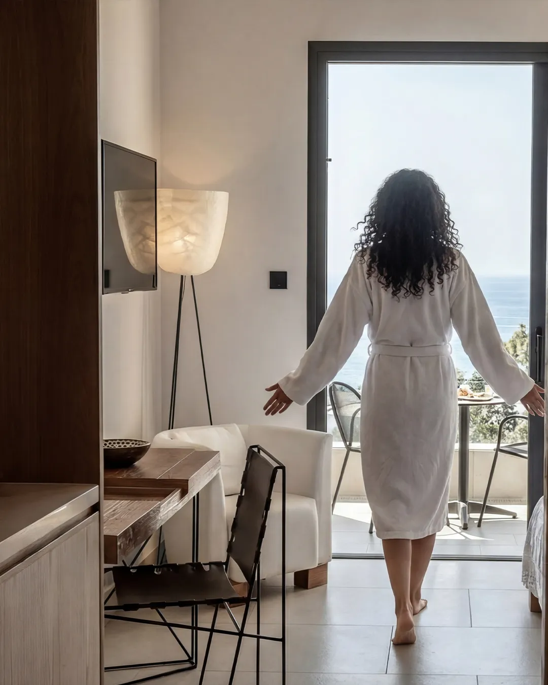 Guest walking toward a sunlit balcony overlooking the Mediterranean